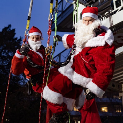 Als Nikoläuse verkleidet hängen zwei Höhenretter der Feuerwehr Köln an einem Seil vor er Uniklinik Köln.