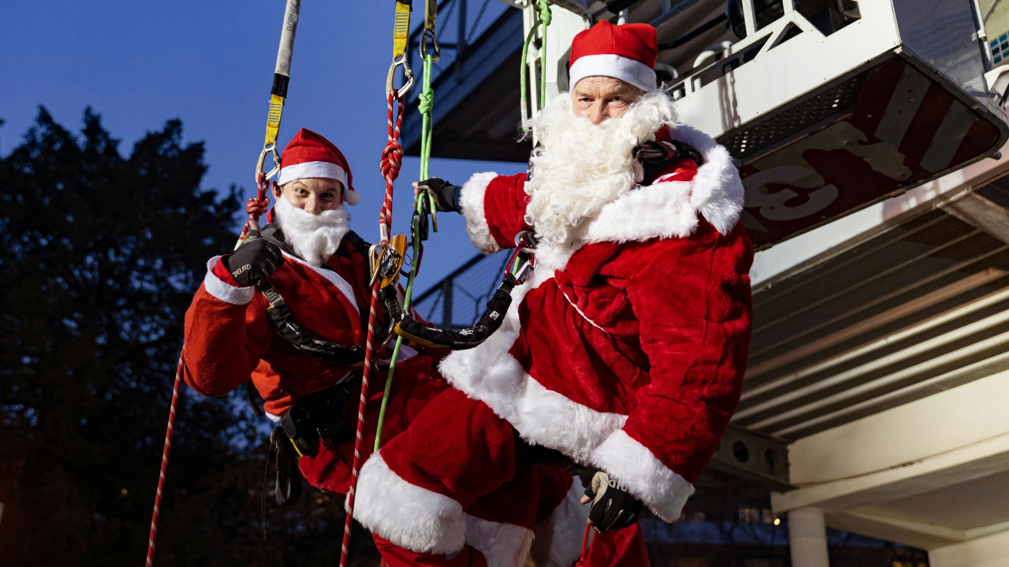 Als Nikoläuse verkleidet hängen zwei Höhenretter der Feuerwehr Köln an einem Seil vor er Uniklinik Köln.