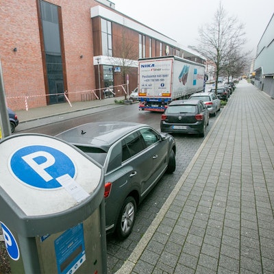 Ein Parkautomat steht am Straßenrand. Autos stehen daneben in Parkbuchten.