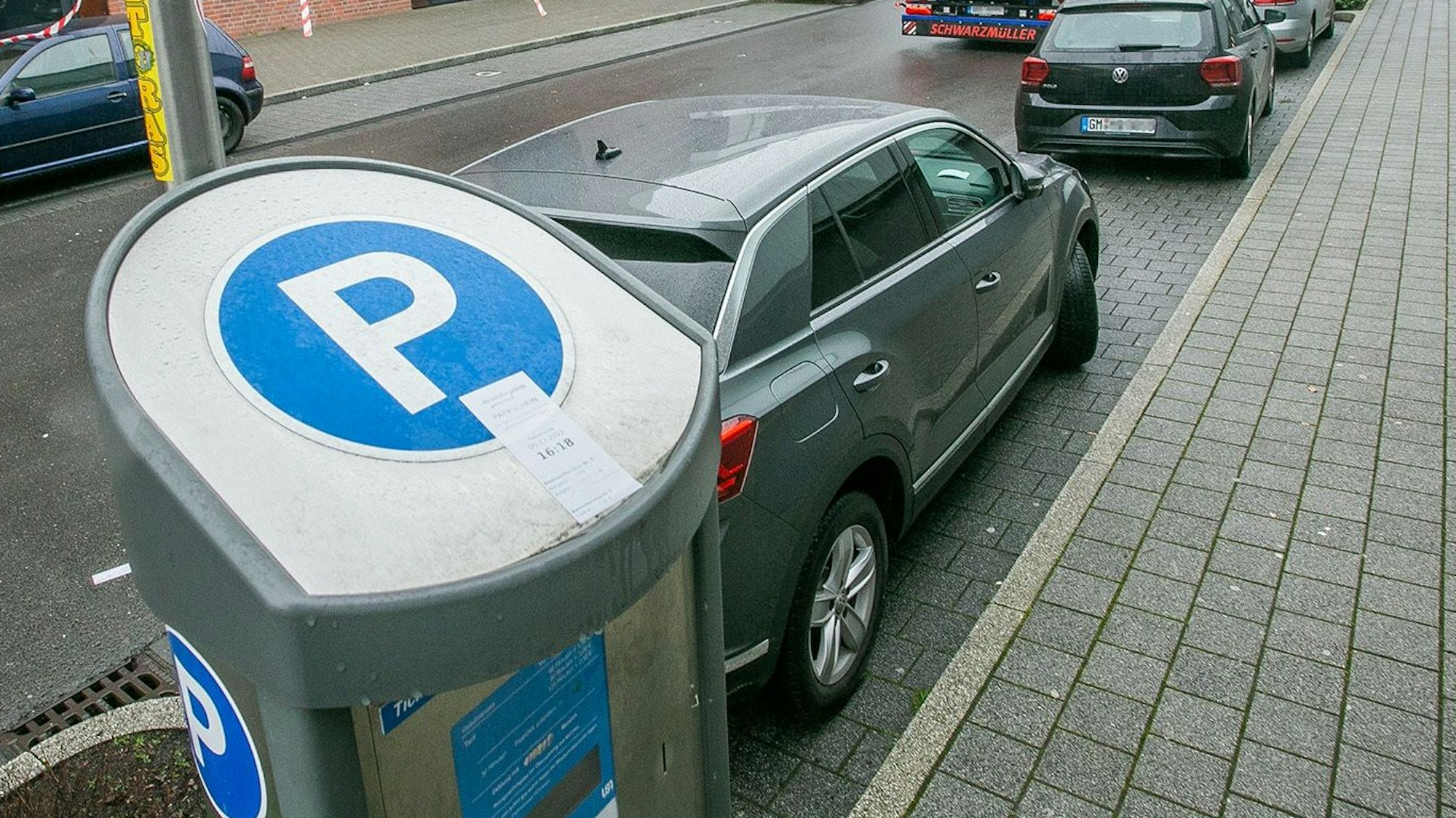 Ein Parkautomat steht am Straßenrand. Autos stehen daneben in Parkbuchten.