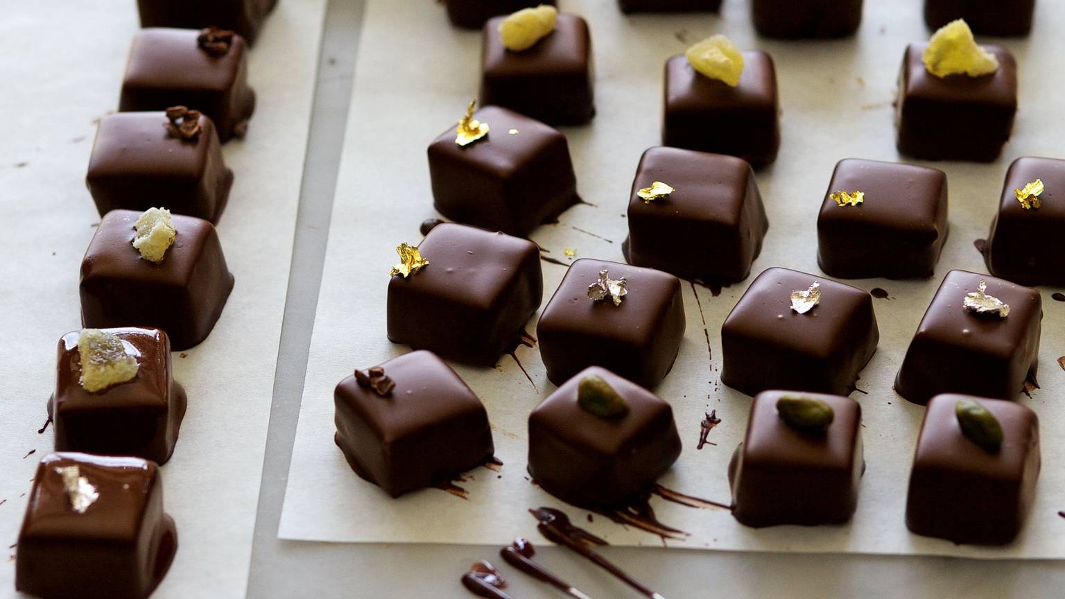 Pralinen liegen auf einem Backpapier, verziert mit Goldblättchen und Nüssen