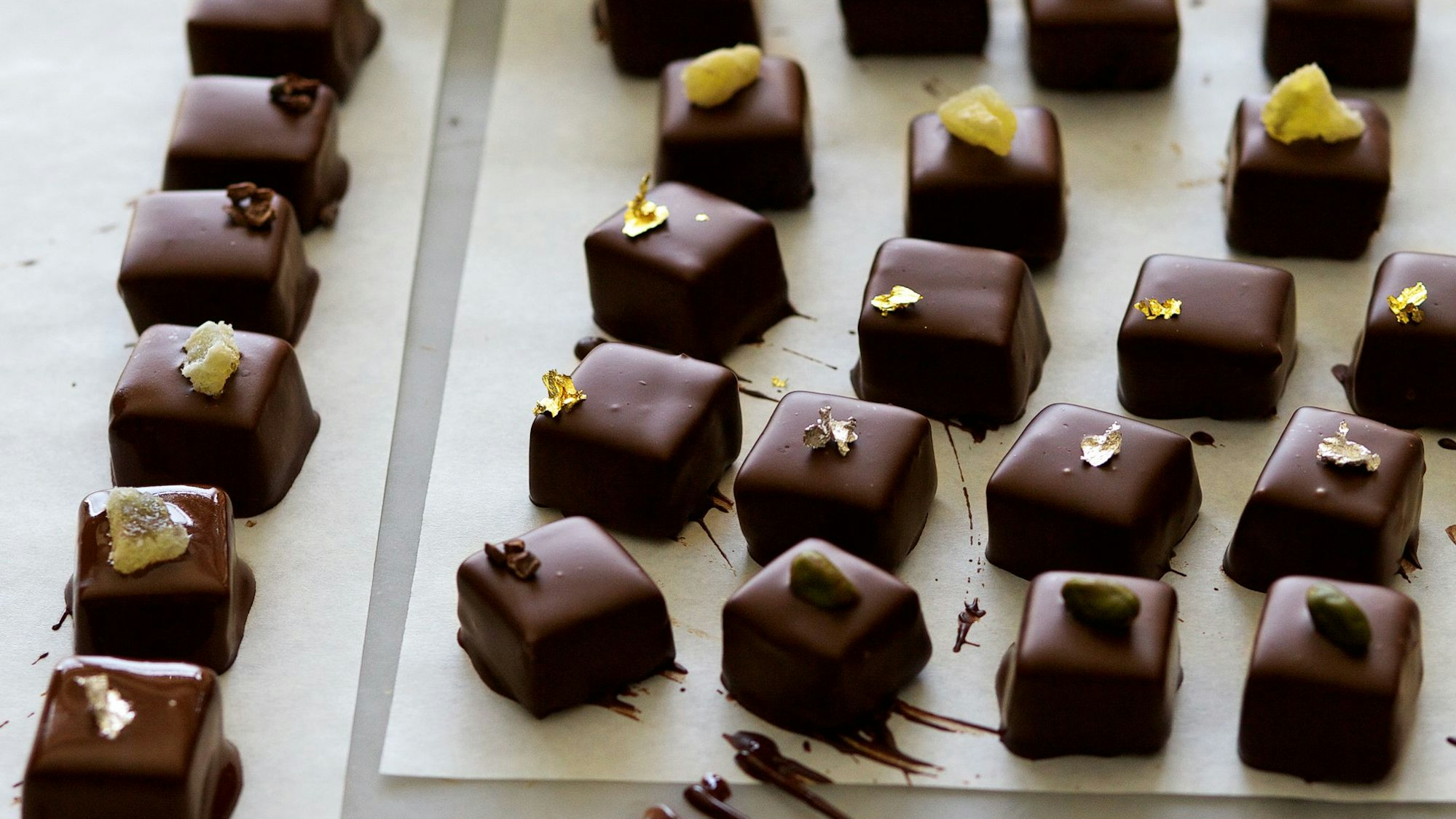 Pralinen liegen auf einem Backpapier, verziert mit Goldblättchen und Nüssen