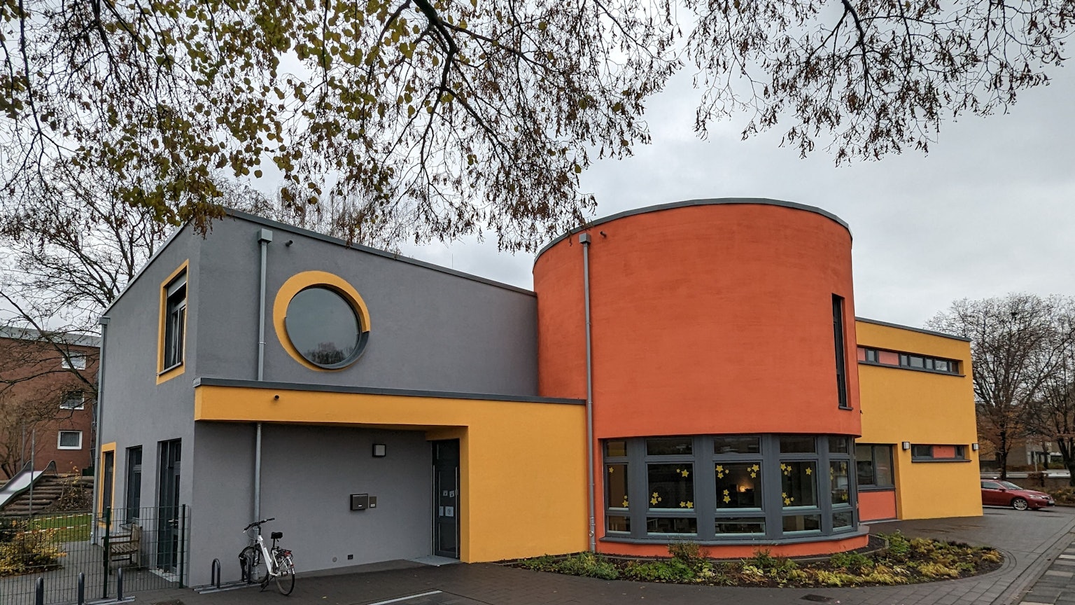 Ein Kita-Gebäude mit grau, gelb und orangen Außenwandfarben.