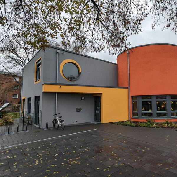 Ein Kita-Gebäude mit grau, gelb und orangen Außenwandfarben.