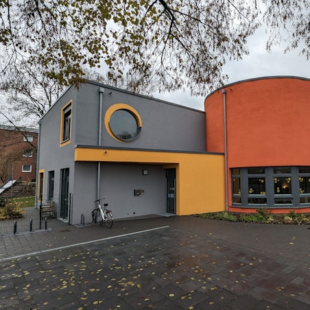 Ein Kita-Gebäude mit grau, gelb und orangen Außenwandfarben.