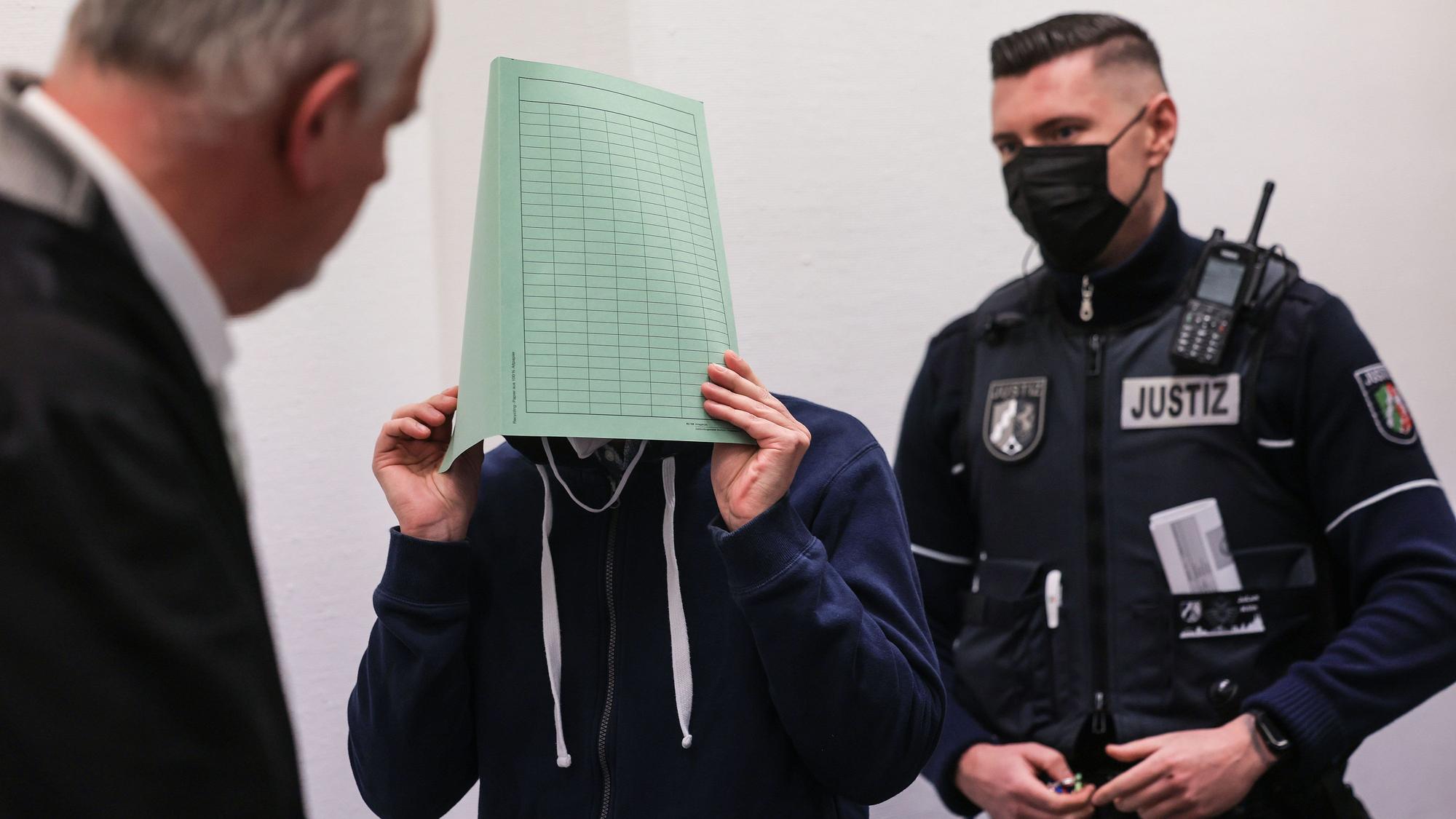 Der Angeklagte (M) im Missbrauchskomplex Wermelskirchen hält sich beim Betreten des Gerichtssaals neben seinem Rechtsanwalt Christian Lange (l) eine Mappe vor das Gesicht. Der Mann soll sich im Internet als Babysitter angeboten und so Kontakt zu den Familien der Opfer bekommen haben. Insgesamt ist er wegen 124 Taten angeklagt, darunter auch Besitz von Kinderpornografie und Beihilfe zum Missbrauch.
