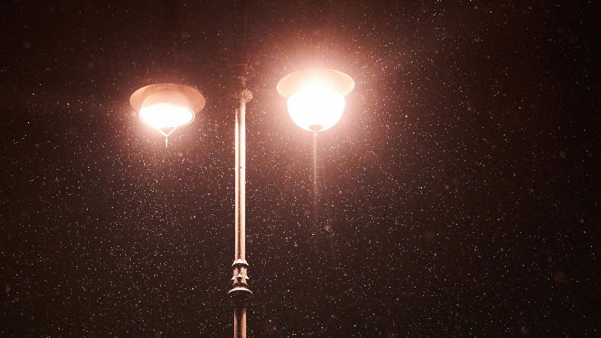 Am frühen Morgen schneit es leicht. Im Lichtschein der Laternen ist Schnee zu sehen.