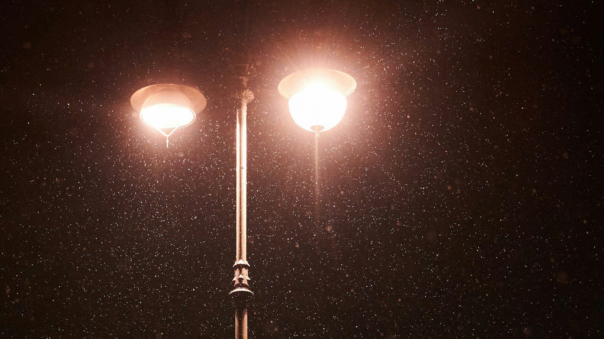 Am frühen Morgen schneit es leicht. Im Lichtschein der Laternen ist Schnee zu sehen.