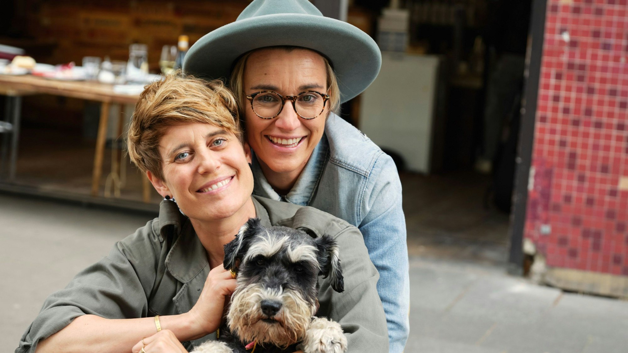 Elli Erl und Tina van Wickeren, van Wickeren hält ihren Hund. sie lächeln in die Kamera.