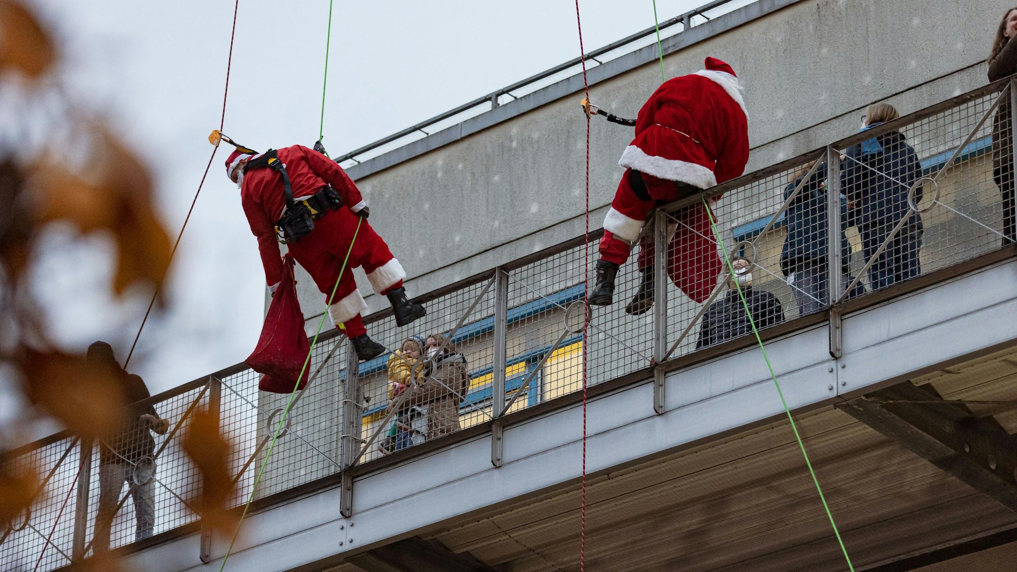 Als Nikoläuse verkleidet hängen zwei Höhenretter der Feuerwehr Köln an einem Seil vor einem Balkon der Kinderklinik der Kölner Uniklinik.