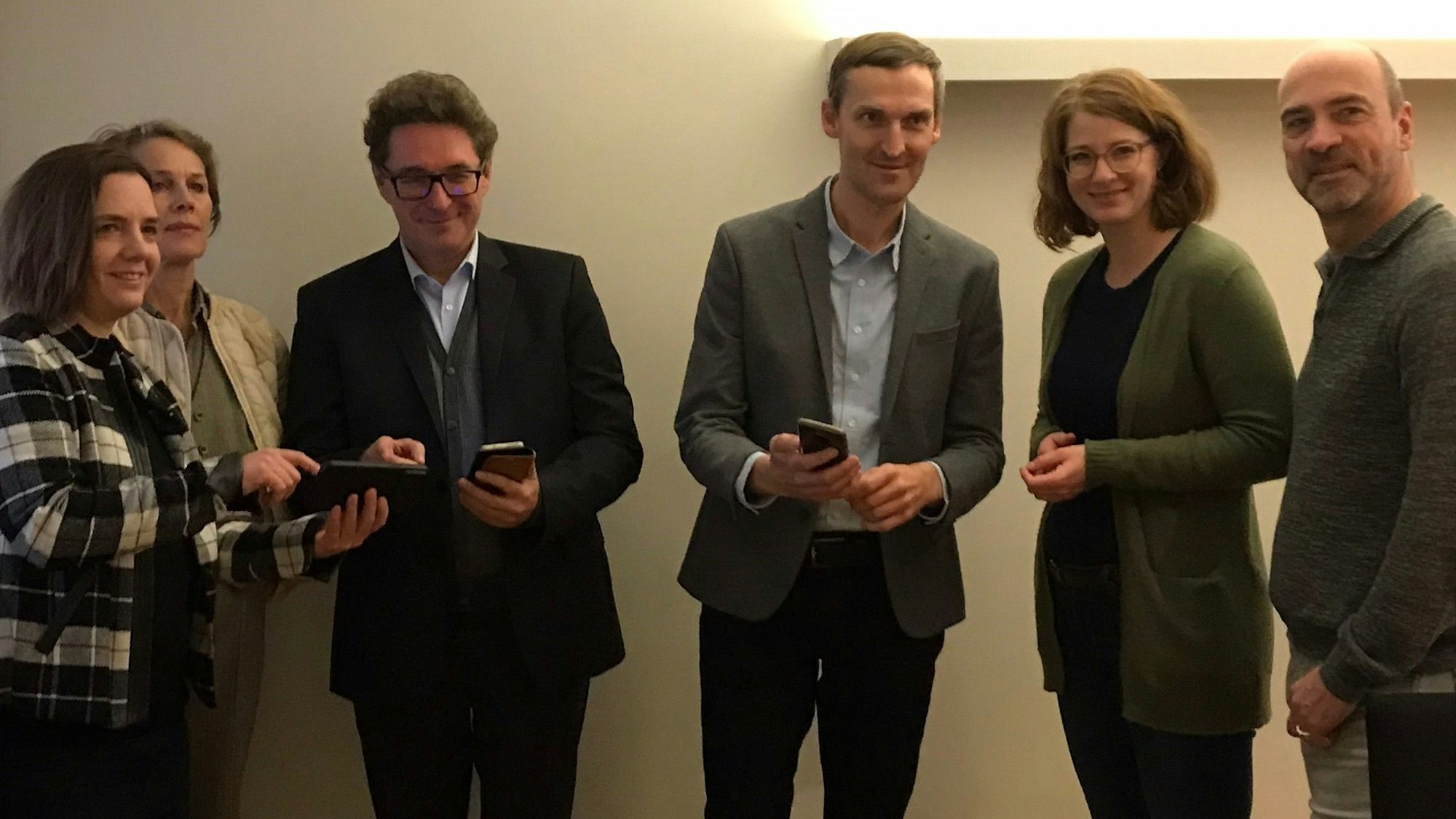 Drei Männer und drei Frauen, die vor einer weißen Wand stehen