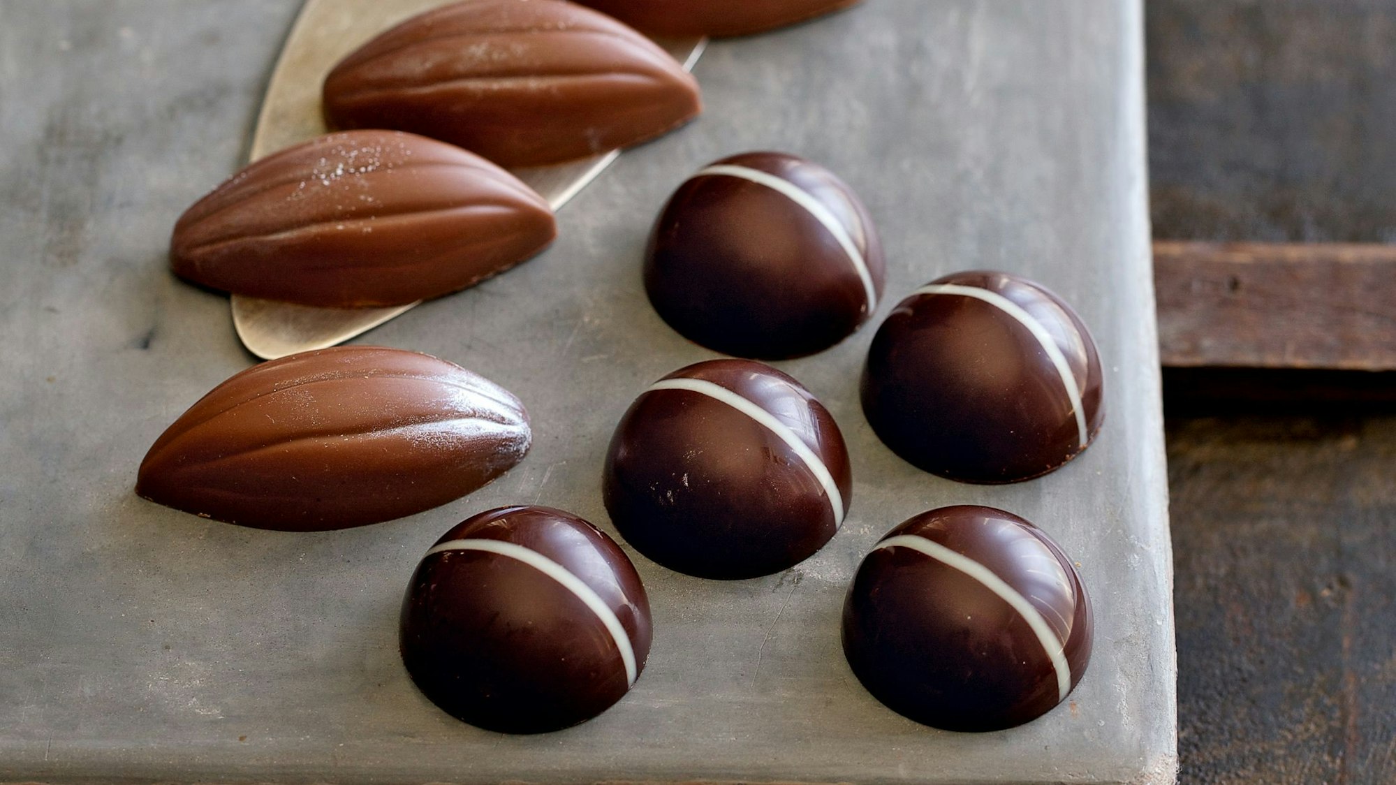 Zwei verschiedene Pralinensorten liegen auf einem Backpapier und sind mit glänzender Konfitüre verziert.