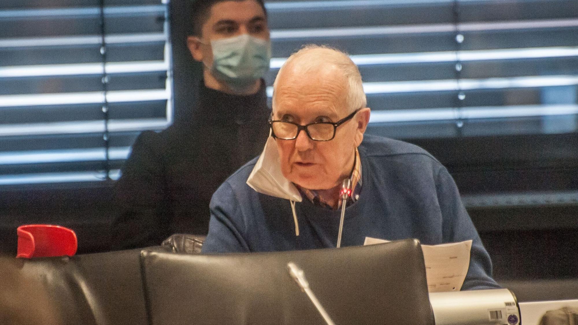 Das Ratsmitglied Erhard Schoofs sitzt im Leverkusener Ratssaal. An seinem rechten Ohr baumelt eine FFP2-Maske.