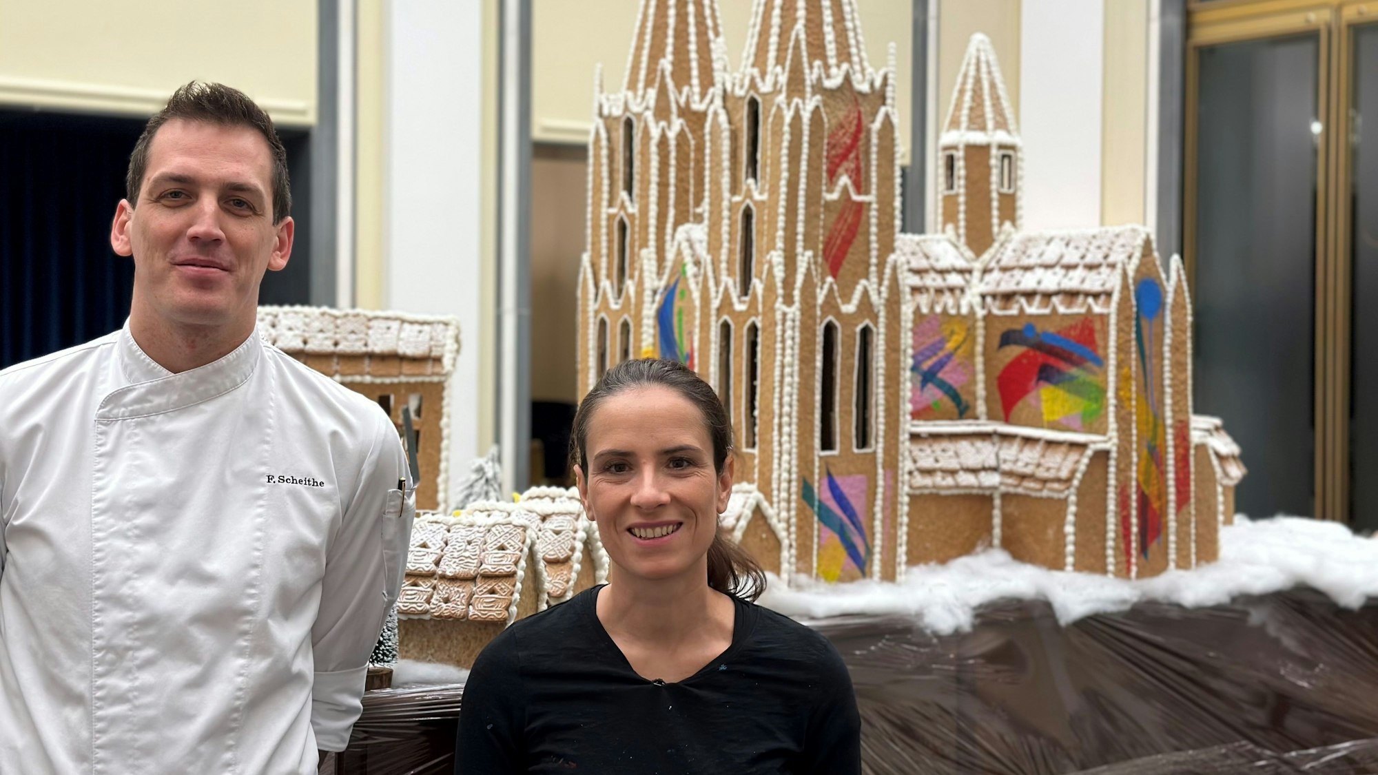 Die Graffiti-Künstlerin Mad C aka Claudia Walde und Patissier Fabian Scheithe stehen vor einem bunt bemalten Dom aus Lebkuchen.