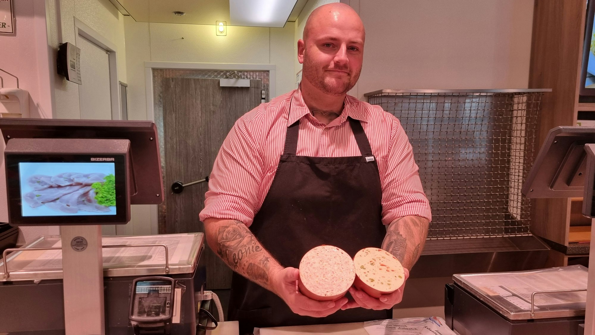 Der Metzgermeister Daniel Pickartz hinter der Theke seiner Metzgerei und hält Wurstwaren in der Hand.