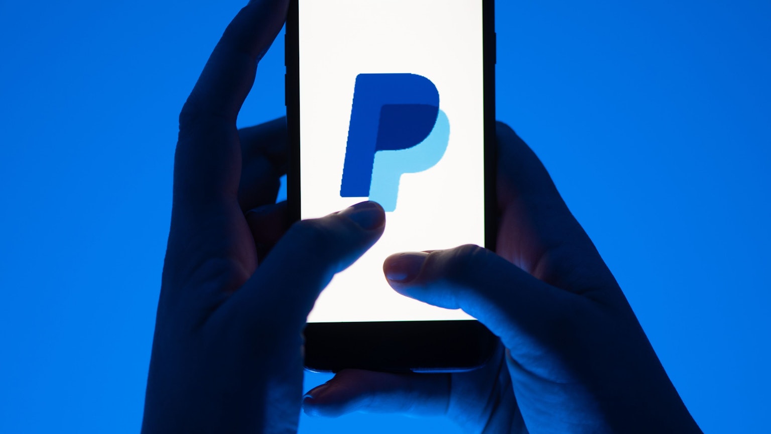 Eine Frau hält ein Smartphone mit dem Logo des Bezahldienst Paypal in der Hand.