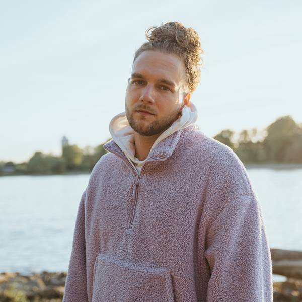 Sänger Wunso steht in einer Fleece-Jacke am Rhein in Köln.
