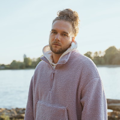 Sänger Wunso steht in einer Fleece-Jacke am Rhein in Köln.