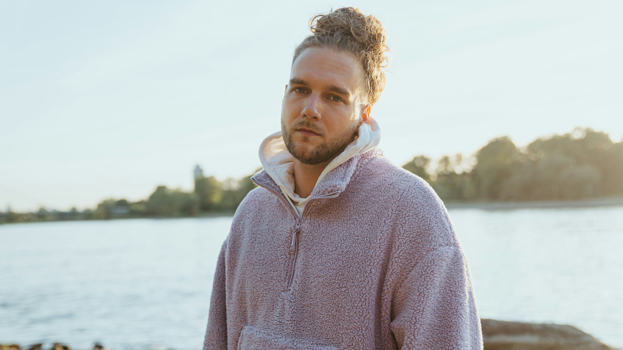 Sänger Wunso steht in einer Fleece-Jacke am Rhein in Köln.