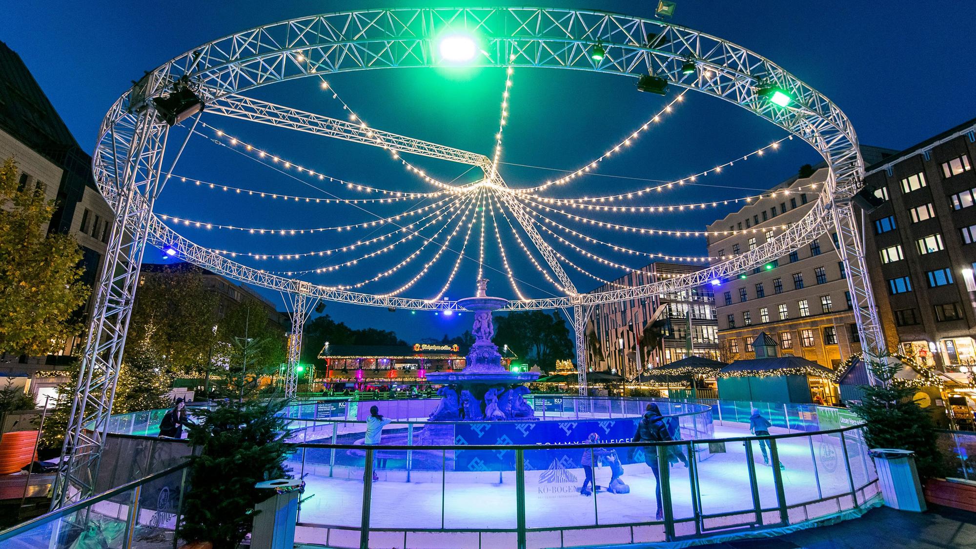 Runde Eisfläche um einen Brunnen, darüber ein Lichterbogen