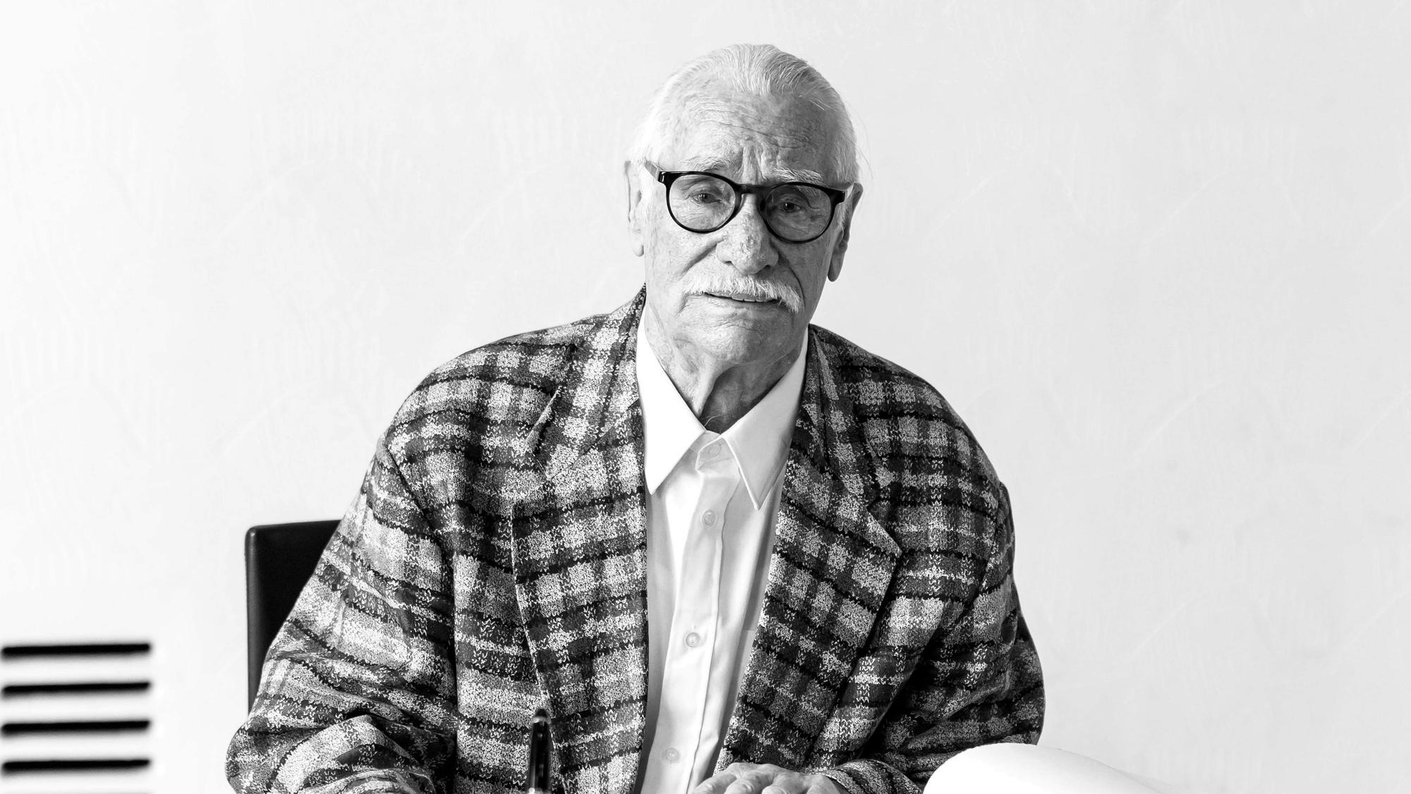 Hans Süper sitzt hinter einem Schreibtisch und schaut in die Kamera.