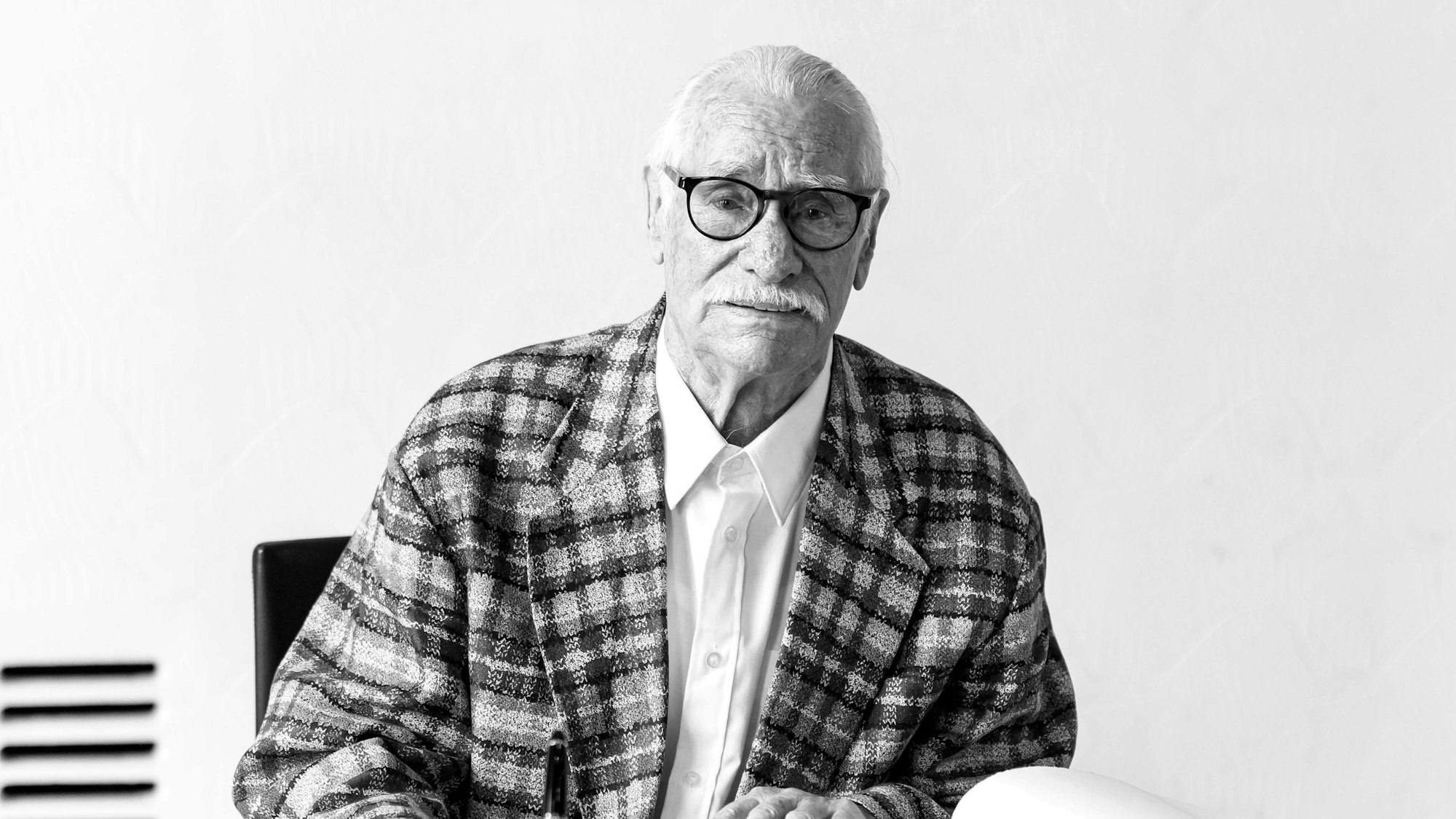 Hans Süper sitzt hinter einem Schreibtisch und schaut in die Kamera.