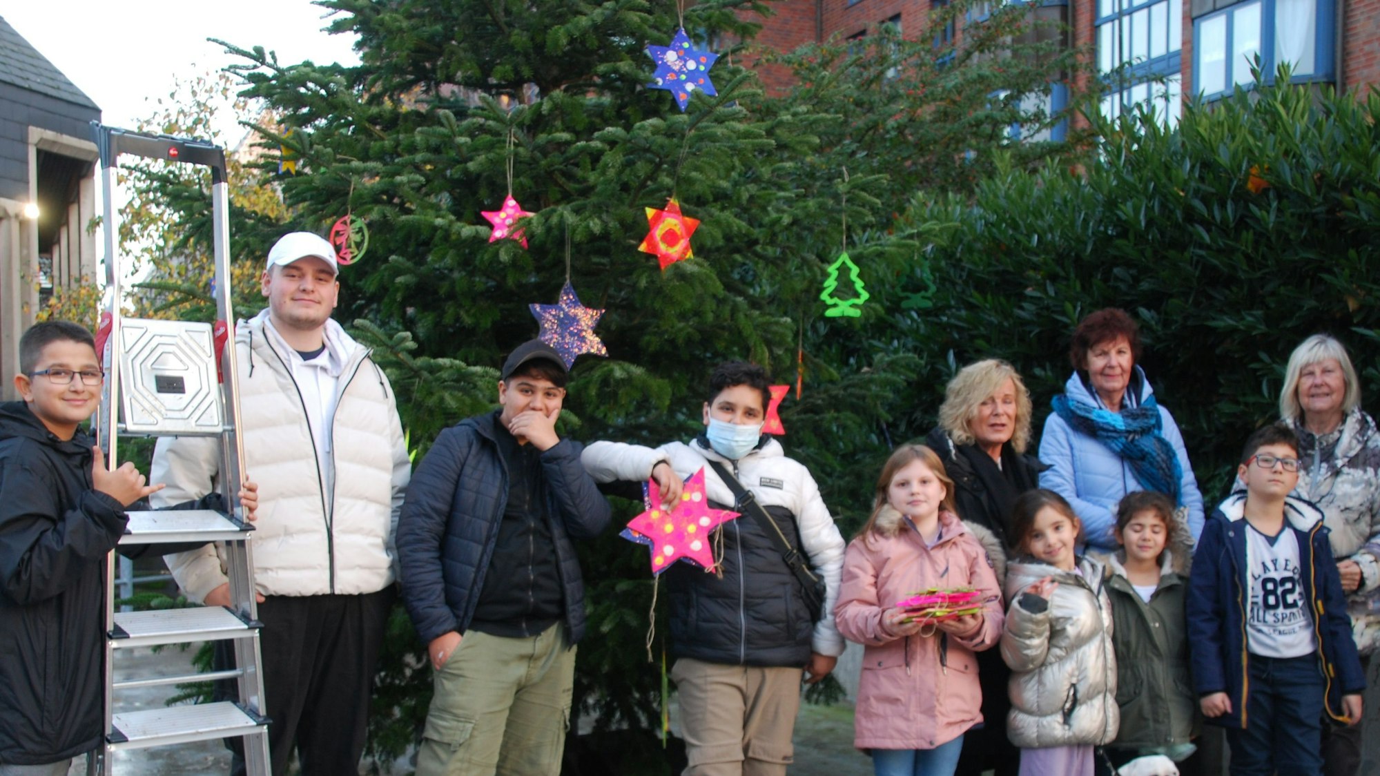 Kinder, Jugendliche und Erwachsene stehen vor einem geschmücken Weihnachtsbaum.