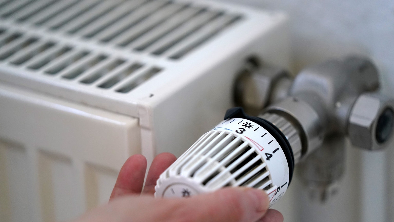 Eine Person dreht an einem Heizungsthermostat.