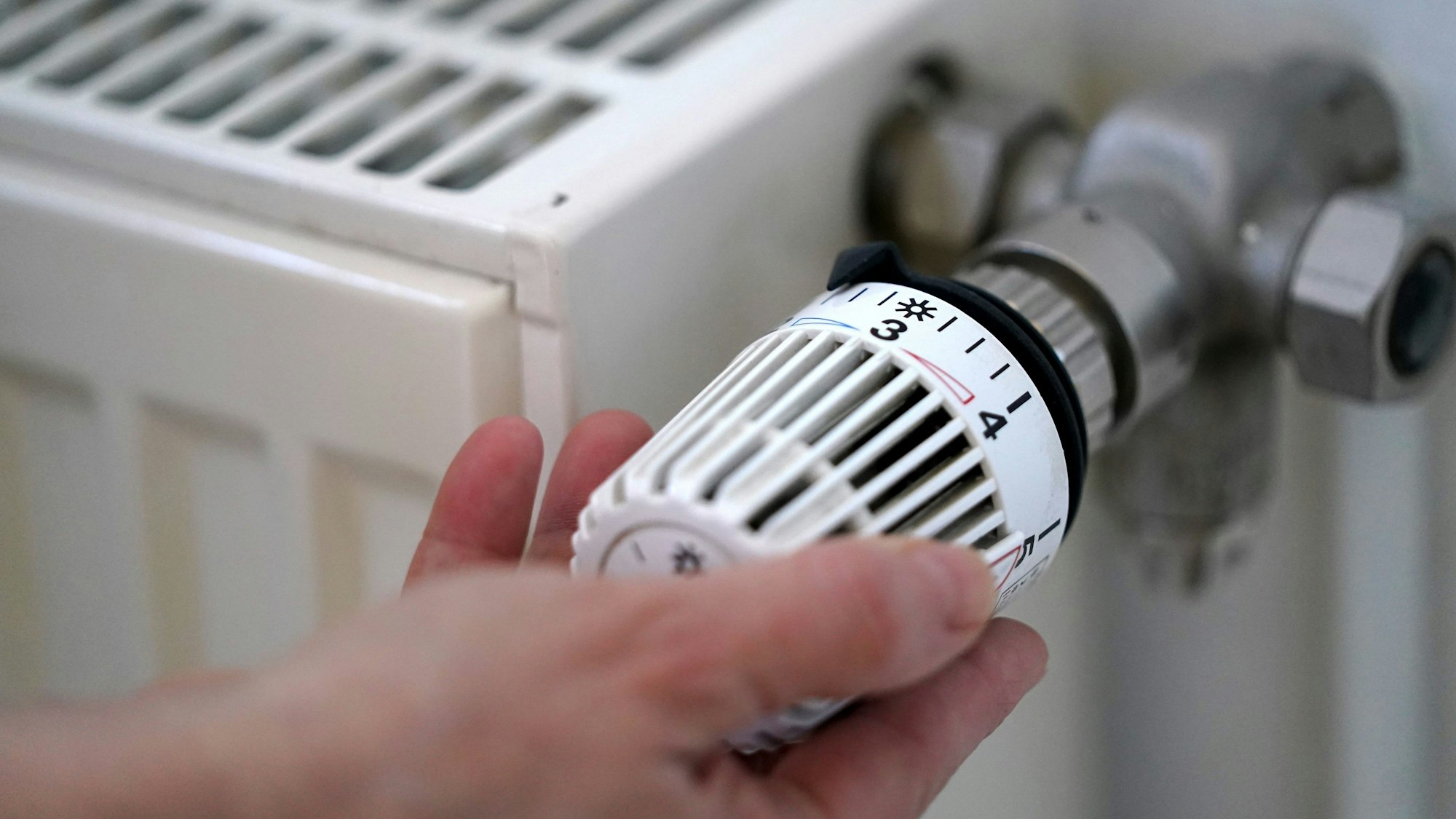 Eine Person dreht an einem Heizungsthermostat.