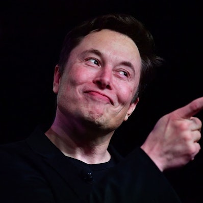 Twitter-Chef Elon Musk steht vor schwarzem Hintergrund, er zeigt mit der rechten Hand.