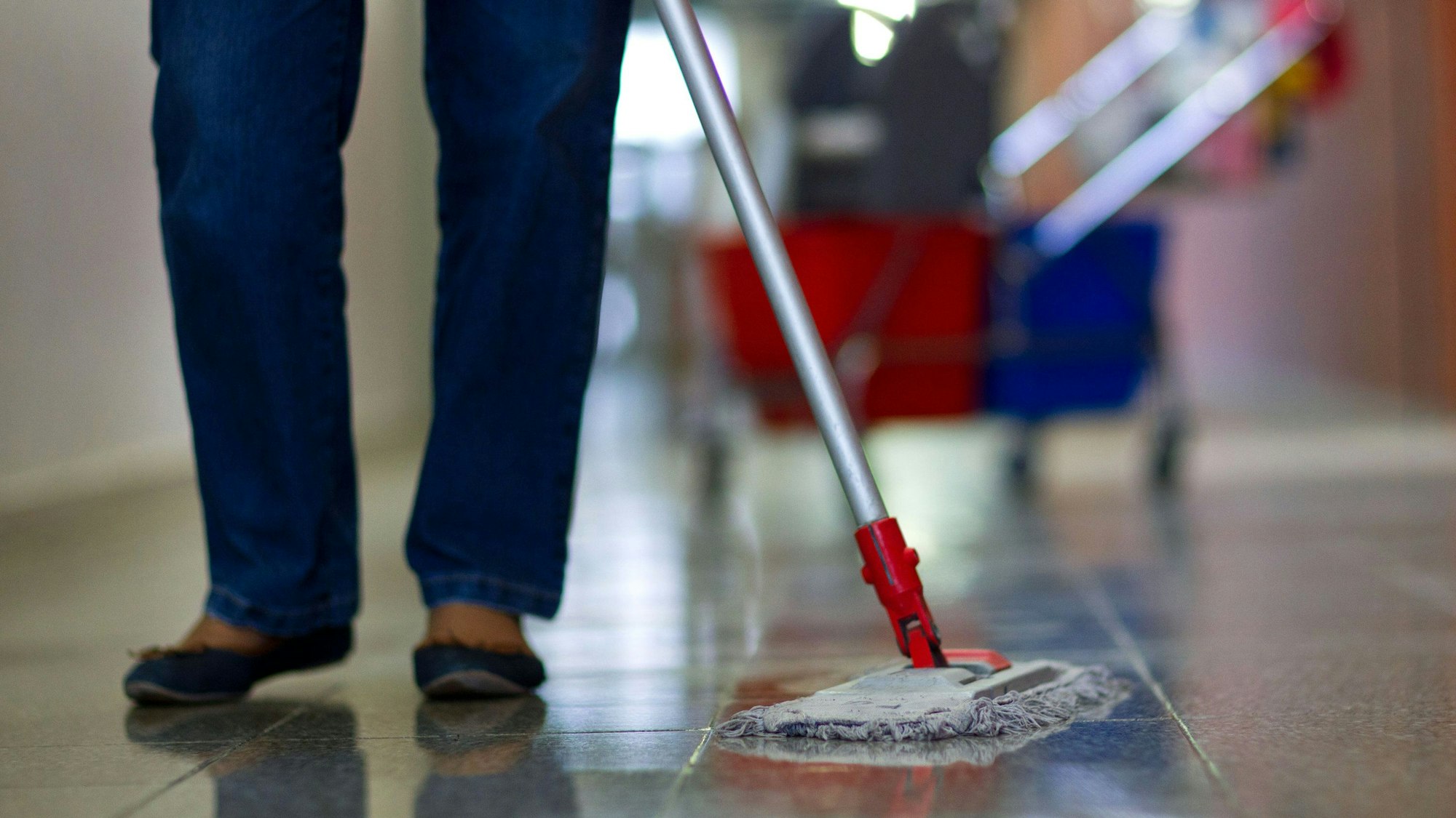 Eine Gebäudereinigerin wischt den Flur in einer Berufsschule.