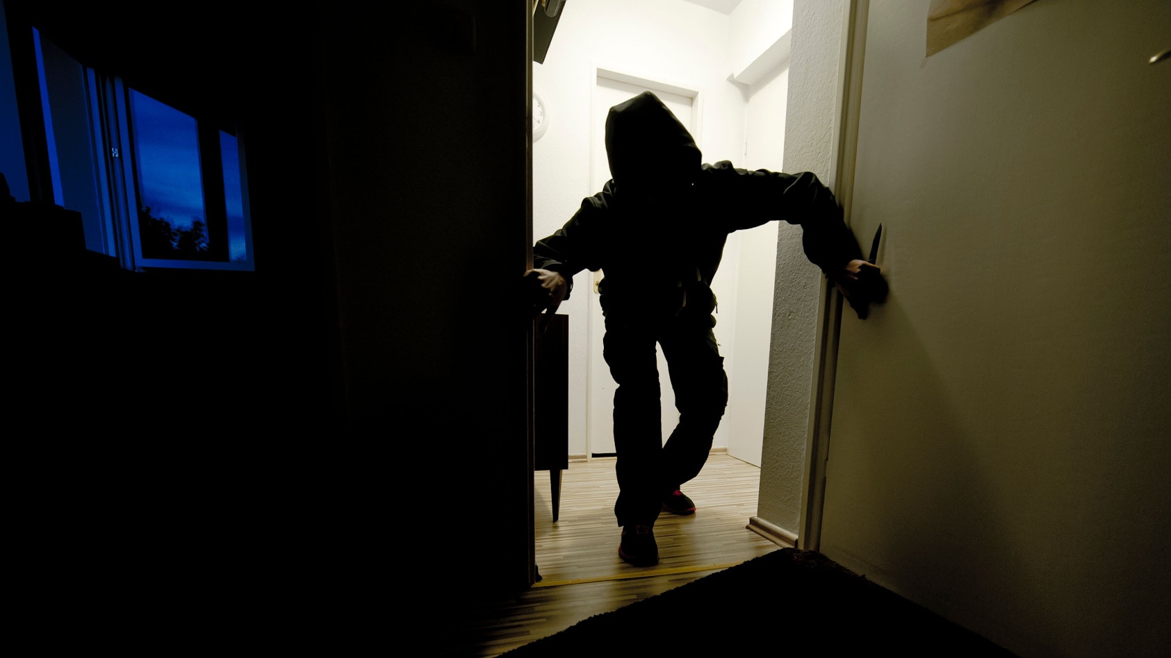 Ein Mann schleicht im Dunkeln durch eine Wohnung.