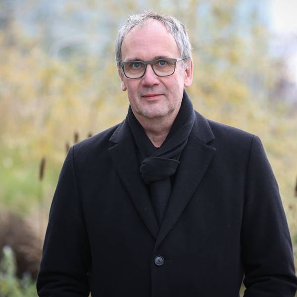 Bestseller-Autor Volker Kutscher steht vor dem Neven DuMont-Haus. Er trägt einen schwarzen Mantel und einen schwarzen Schal.