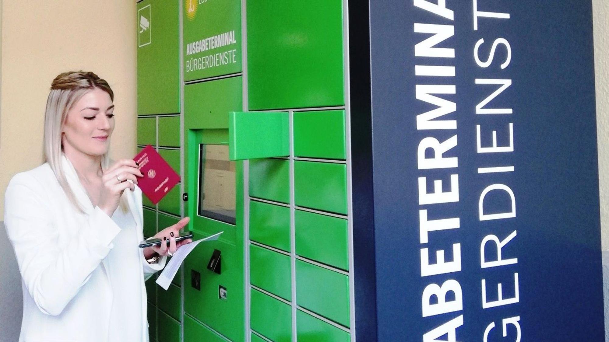 Eine Frau entnimmt einen Reisepass aus dem Schließfach eines Ausweisterminals.