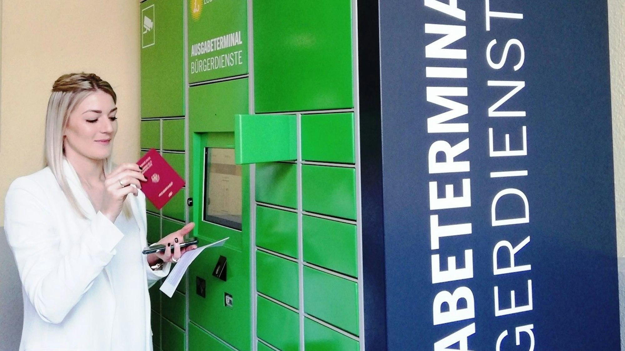 Eine Frau entnimmt einen Reisepass aus dem Schließfach eines Ausweisterminals.