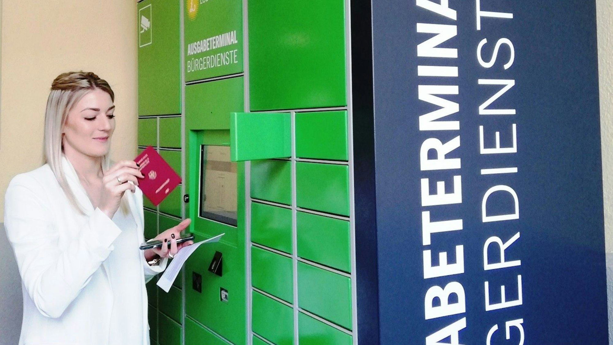 Eine Frau entnimmt einen Reisepass aus dem Schließfach eines Ausweisterminals.
