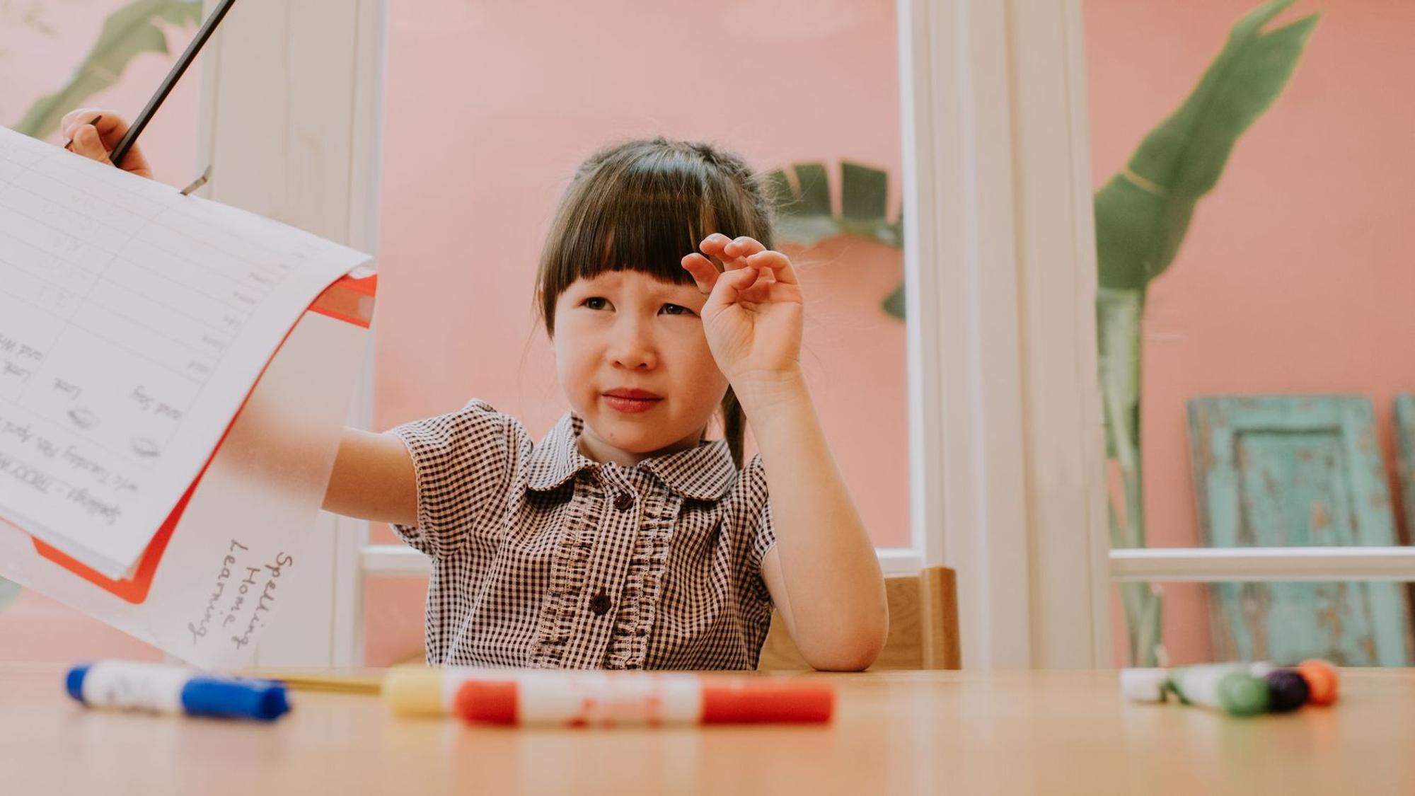 Ein Grundschul-Mädchen hält verzweifelt eine Schulaufgabe in die Höhe, es scheint Probleme mit der Lösung zu haben.