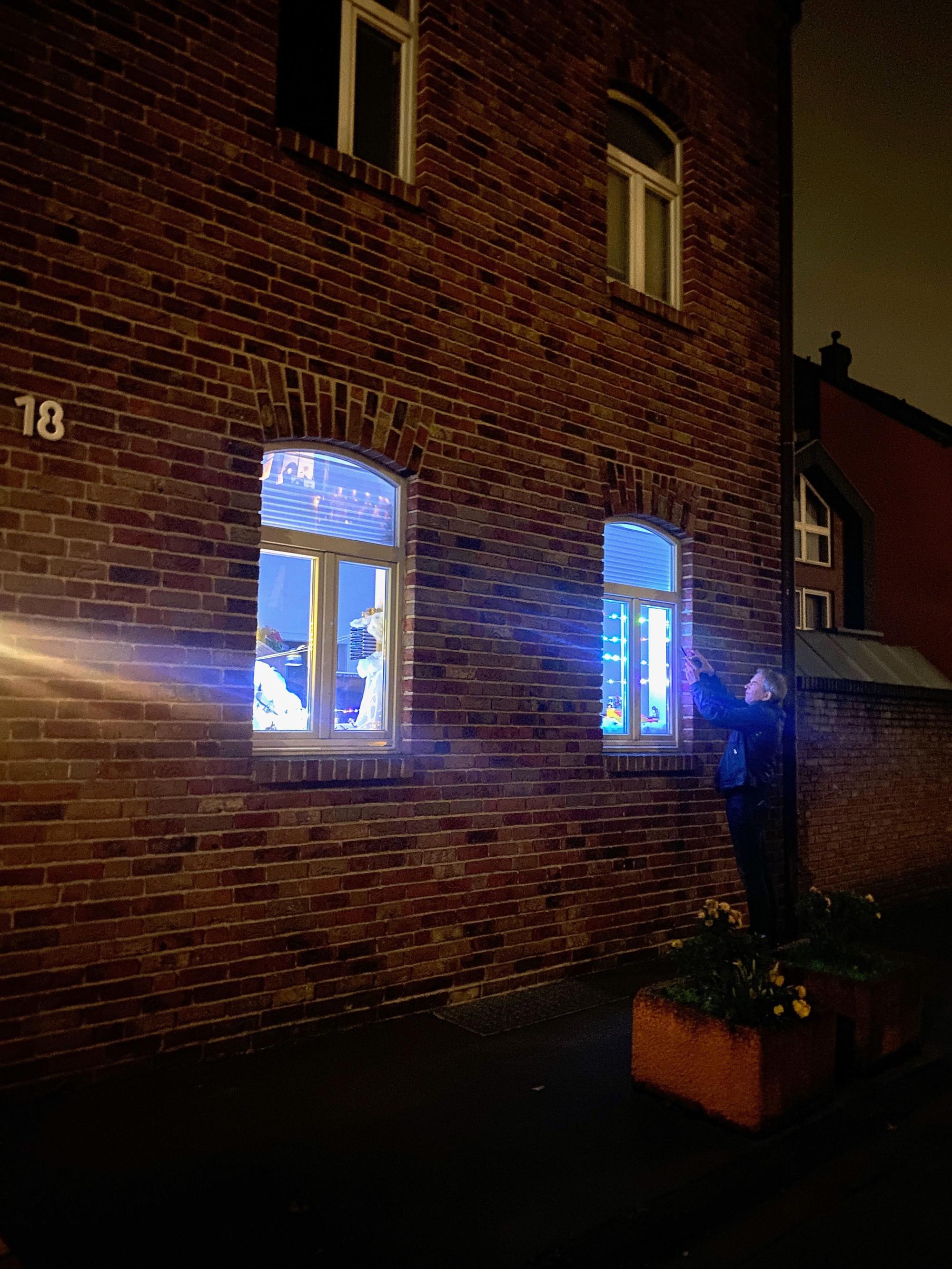 Ein Mann fotografiert von außen eins der erleuchteten und als Lego-Landschaft dekorierten Fenster an einer nächtlichen Straße.