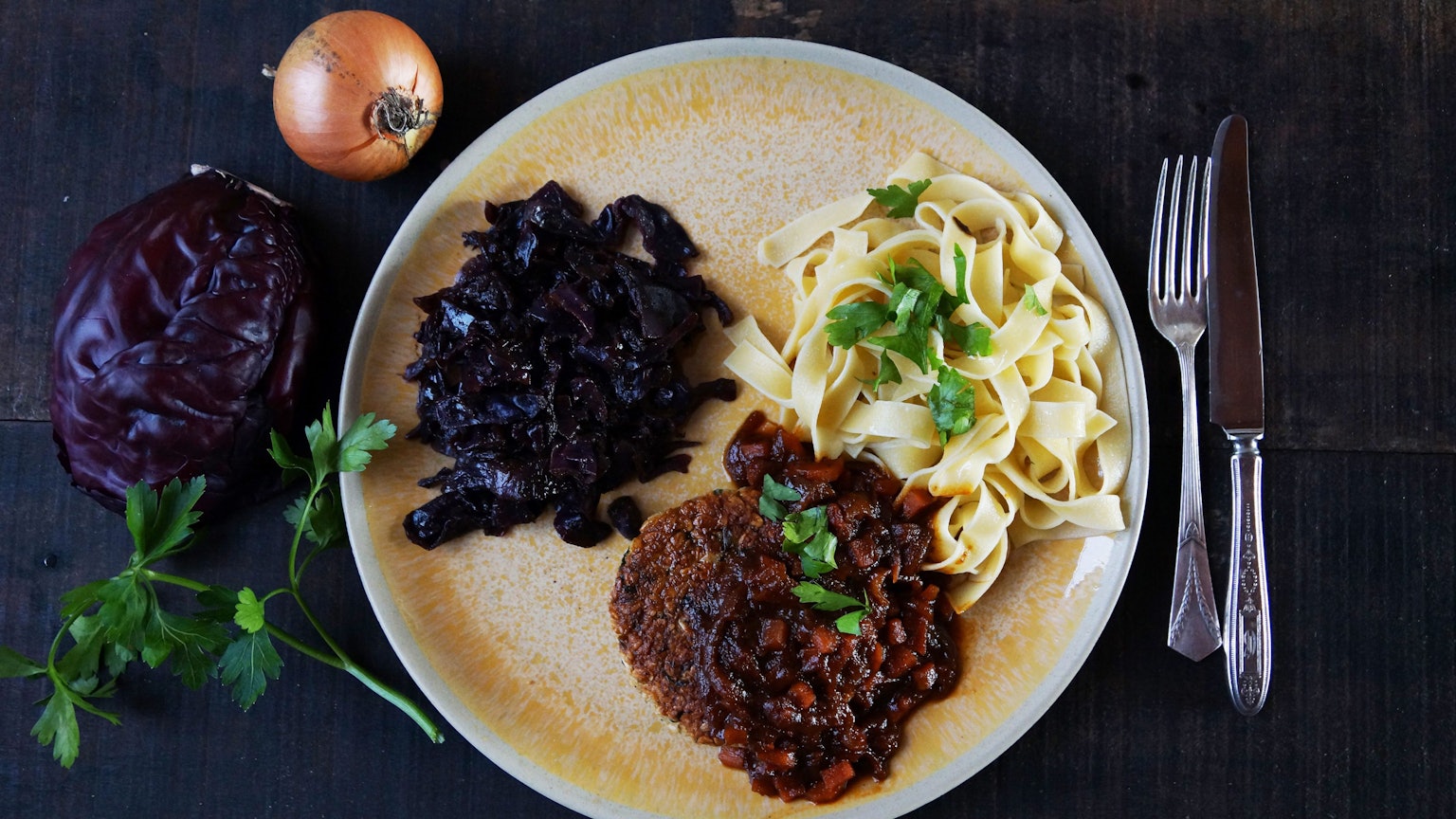 Ein luftiges Tagliatelle-Knäuel bildet mit weihnachtlichem Rotkraut und der krossen Veggie-Frikadelle ein Trio auf dem Teller.