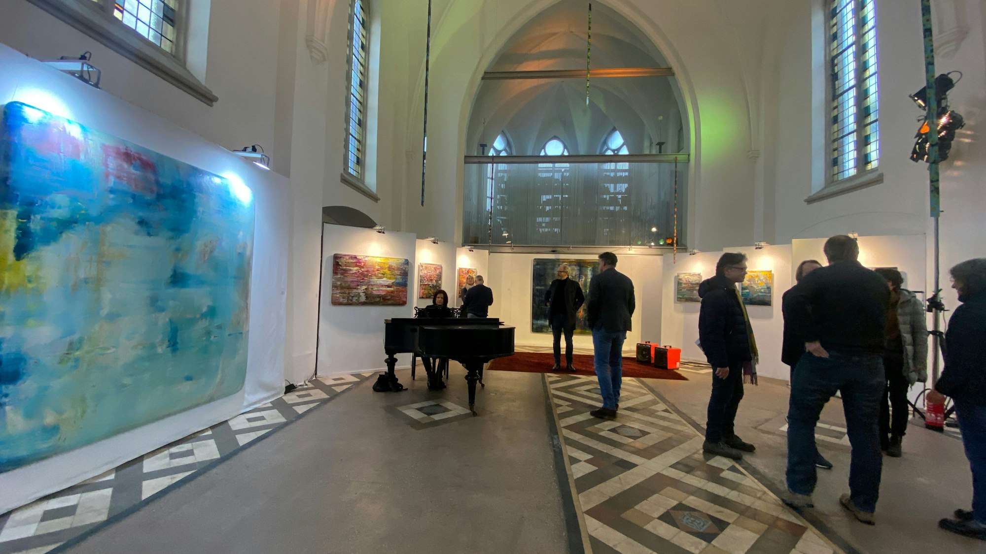 In einem Kirchenraum stehen einige Besucher, an den Wänden hängen groß- und kleinformatige Bilder.