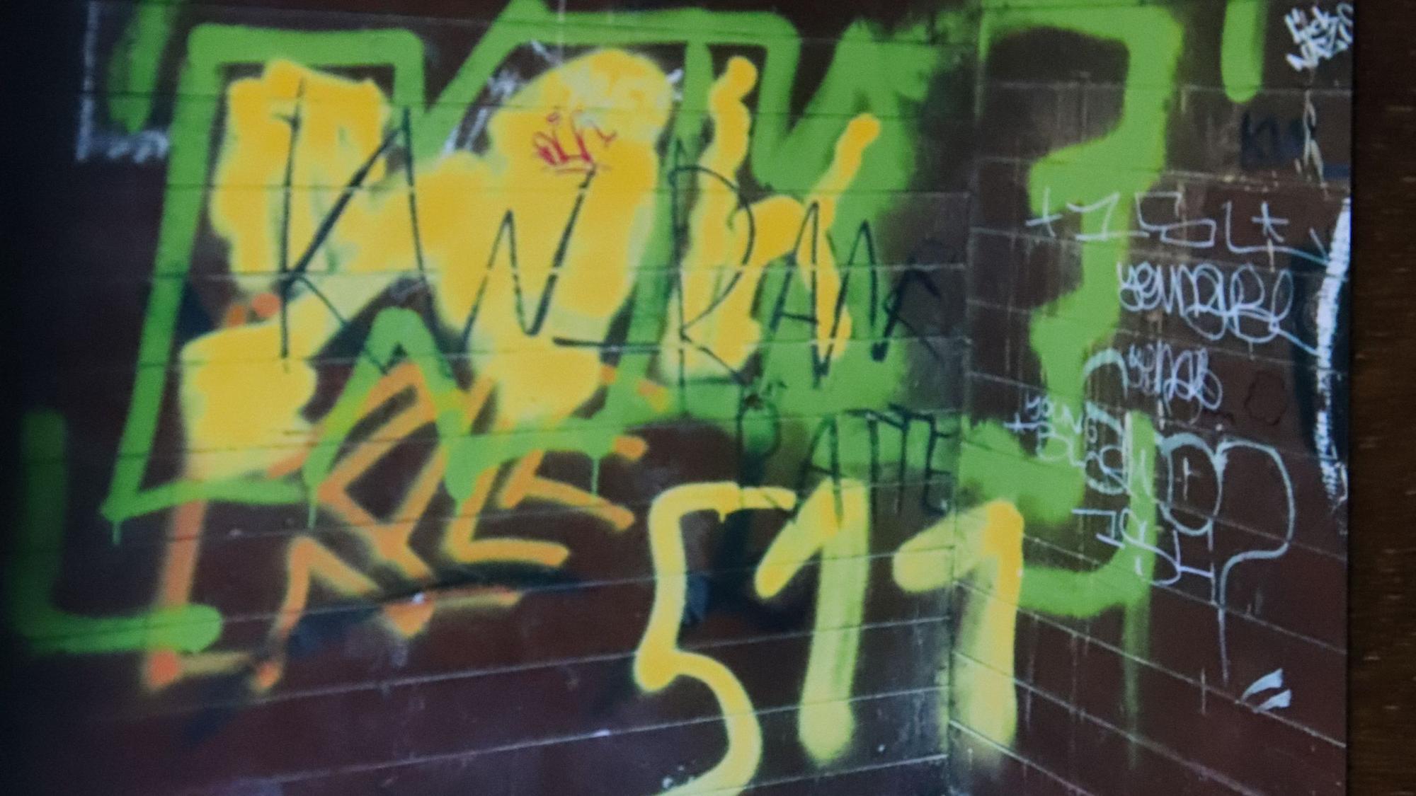 Die Wände des Bushäuschens sind in grün-gelber Schrift mit Graffiti beschmiert.