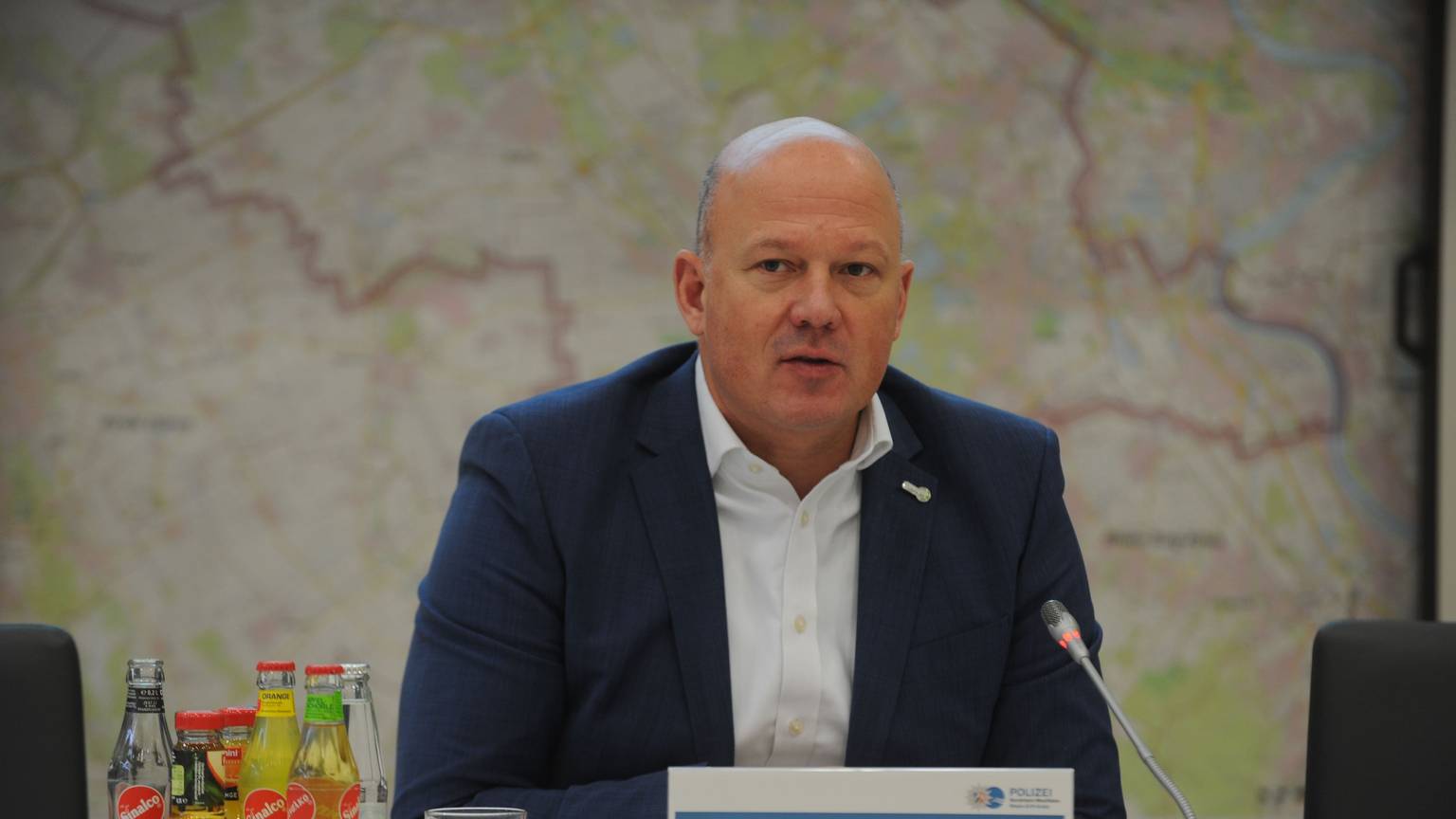 Landrat Frank Rock sitzt während einer Pressekonferenz im Sitzungssaal des Kreishauses und spricht in ein Mikrofon.