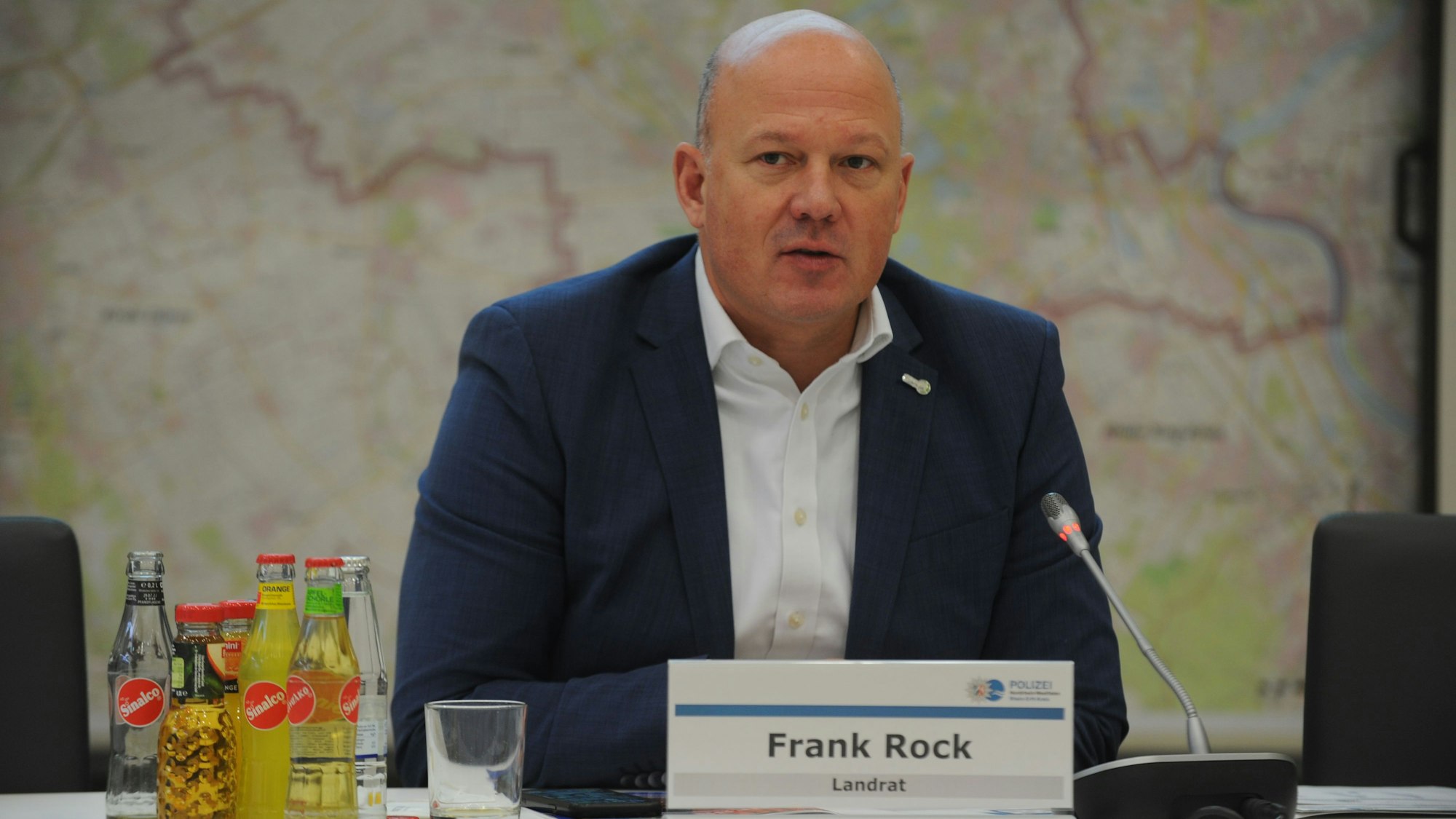 Landrat Frank Rock sitzt während einer Pressekonferenz im Sitzungssaal des Kreishauses und spricht in ein Mikrofon.