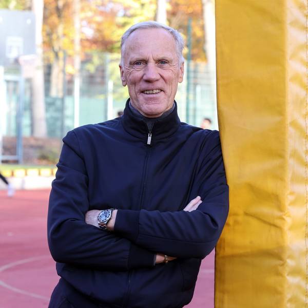 Der Kölner Sportprofessor Ingo Froböse steht auf einem Sportplatz und guckt in die Kamera.