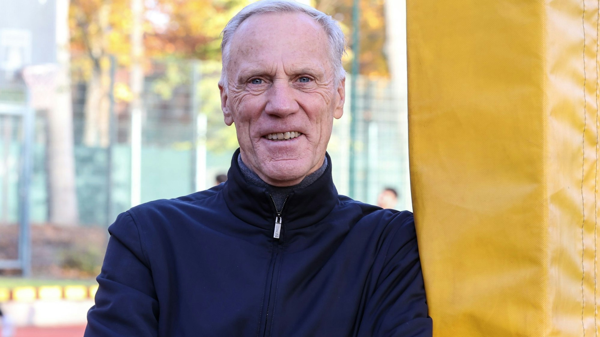 Der Kölner Sportprofessor Ingo Froböse steht auf einem Sportplatz und guckt in die Kamera.