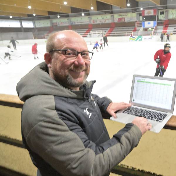 Peter Schüller, Vorstandsmitglied des Eissportvereins Bergisch Gladbach, steht mit Laptop am Rand der Eisbahn, während darauf Jugendliche Eishockey spielen.