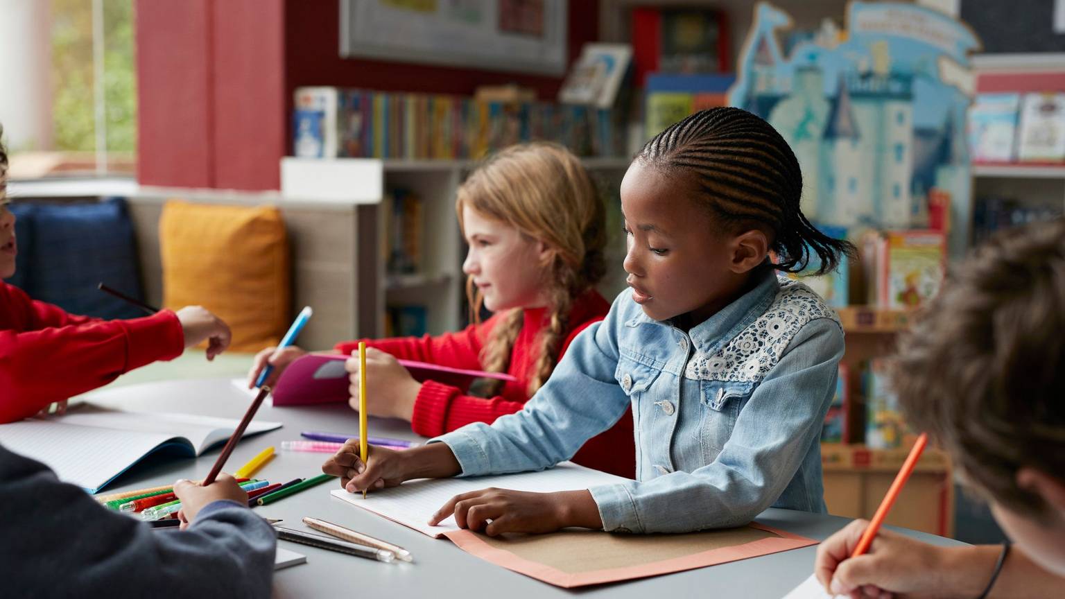 Drei Schulkinder sitzen in einem Klassenraum, in der Mitte ein schwarzes Mädchen.