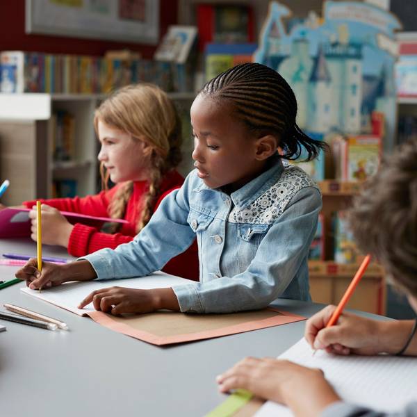 Drei Schulkinder sitzen in einem Klassenraum, in der Mitte ein schwarzes Mädchen.