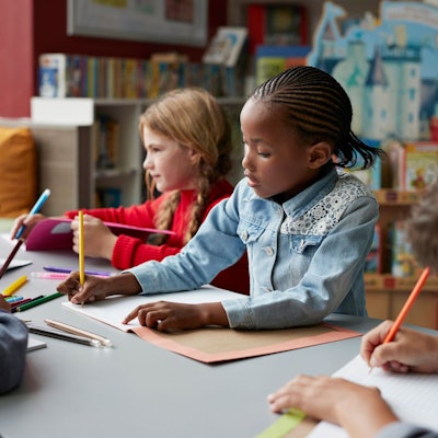 Drei Schulkinder sitzen in einem Klassenraum, in der Mitte ein schwarzes Mädchen.