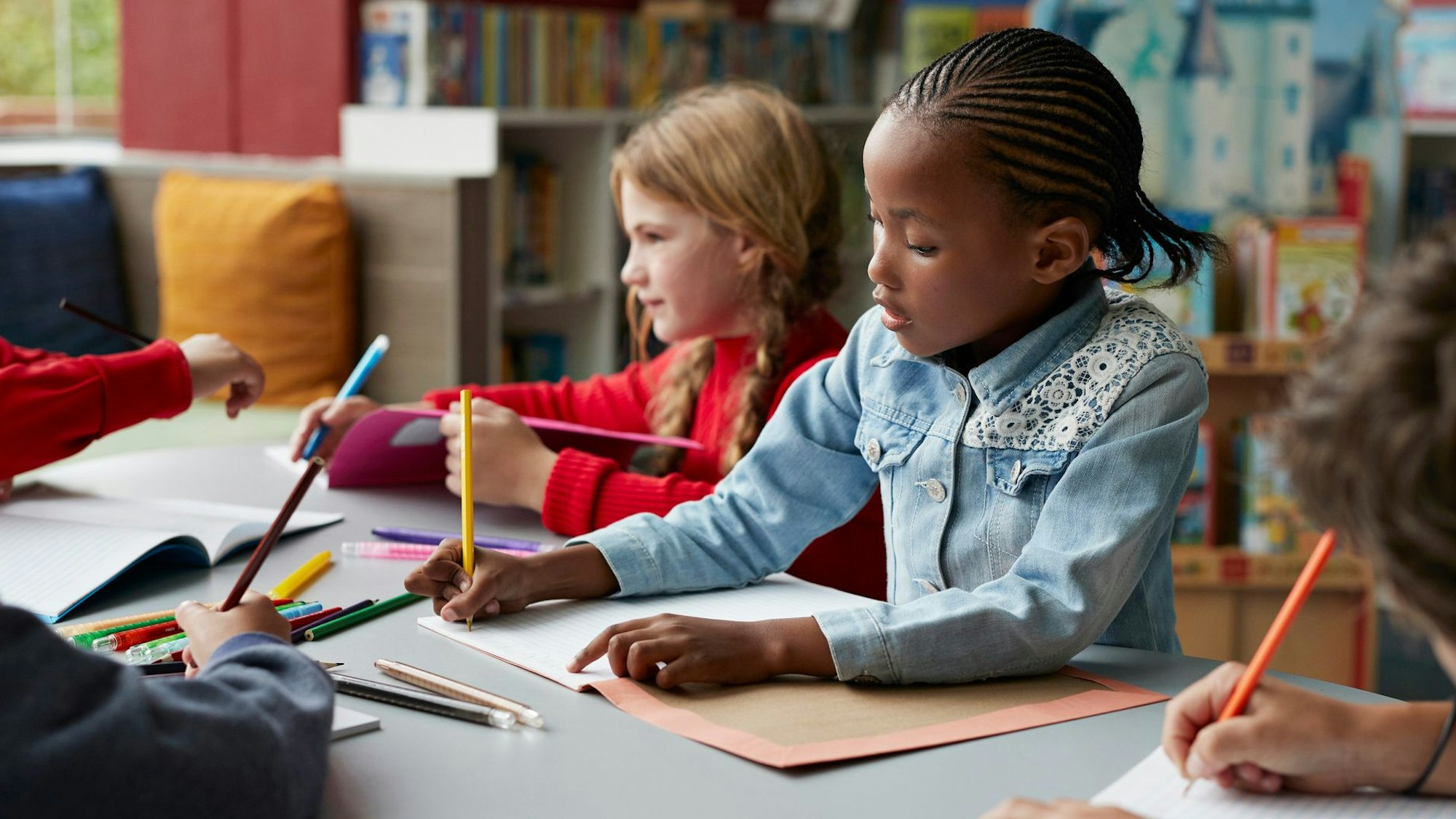Drei Schulkinder sitzen in einem Klassenraum, in der Mitte ein schwarzes Mädchen.